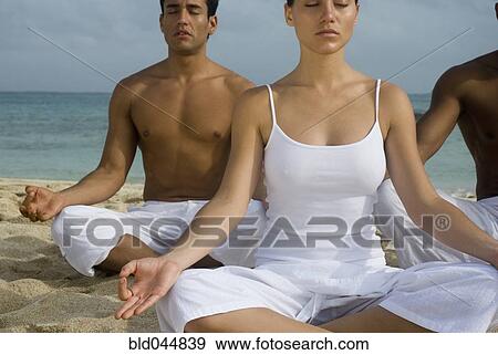 Stock Photo - Multi-ethnic friends meditating on beach. Fotosearch