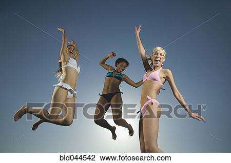 Stock Image - Multi-ethnic women in bathing suits jumping. Fotosearch