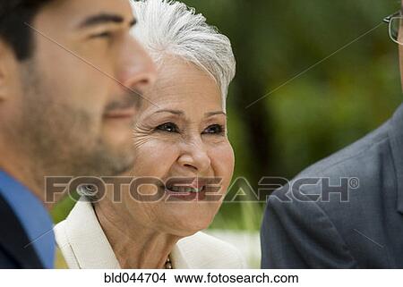 Picture - Senior Hispanic businesswoman next to businessmen. Fotosearch