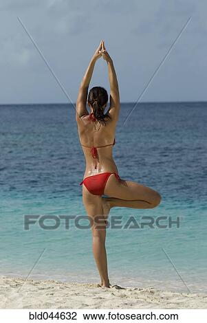 Stock Image - Young woman practicing yoga at beach. Fotosearch