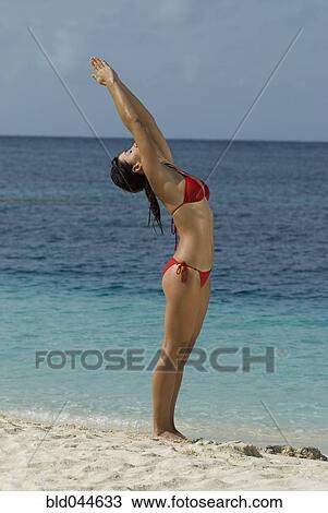 Stock Image - Young woman practicing yoga at beach. Fotosearch