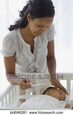 Stock Image - African American mother checking baby’s temperature. Fotosearch