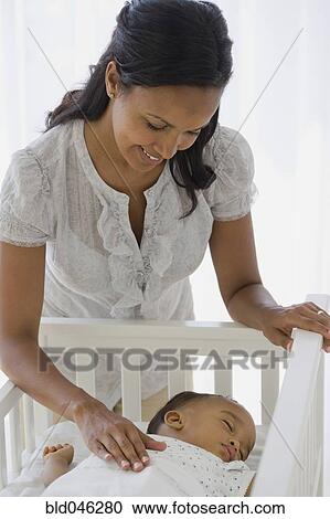 Stock Image - African American mother watching baby sleep. Fotosearch