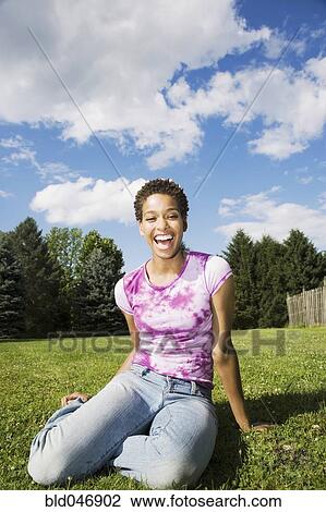 Stock Image - African American woman sitting in grass. Fotosearch