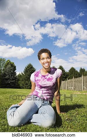Stock Image - African American woman sitting in grass. Fotosearch