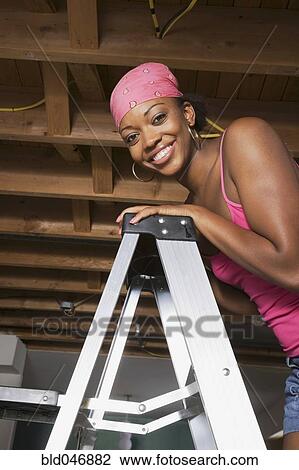 Stock Image - African woman standing on ladder. Fotosearch