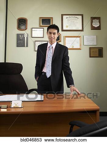 Stock Image - Asian businessman leaning on desk. Fotosearch