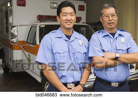 Stock Image - Asian male paramedics in front of ambulance. Fotosearch