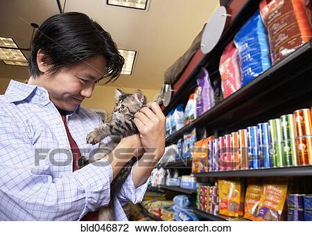 Stock Image - Asian man holding kitten in pet store. Fotosearch