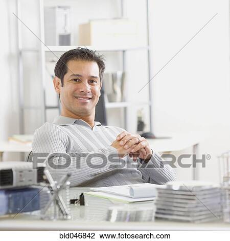 Hispanic man sitting at desk View Large Photo Image Stock Image - Hispanic man sitting at desk. Fotosearch