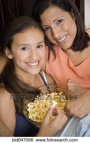 Stock Photograph - Hispanic mother and daughter eating popcorn. Fotosearch