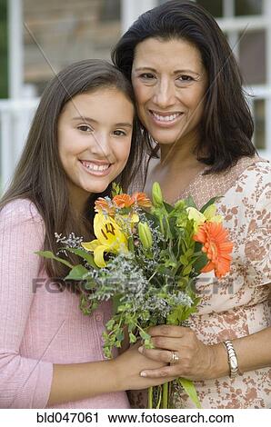 Stock Image - Hispanic mother and daughter holding flowers. Fotosearch