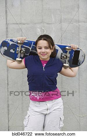 Stock Image - Mixed Race girl holding skateboard. Fotosearch