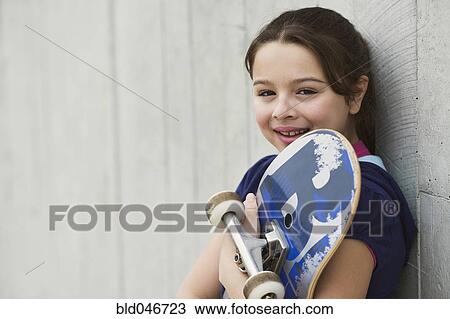 Stock Image - Mixed Race girl holding skateboard. Fotosearch