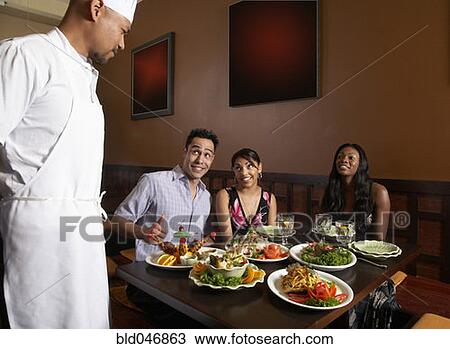 Stock Image - Multi-ethnic friends complimenting chef. Fotosearch