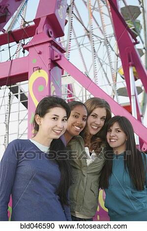 Stock Image - Multi-ethnic girls in front of Ferris wheel. Fotosearch