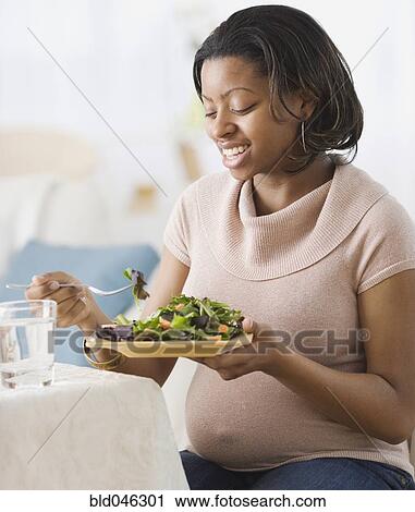 Stock Image - Pregnant African American woman eating salad. Fotosearch