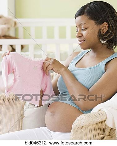 Stock Image - Pregnant African American woman holding baby clothes. Fotosearch