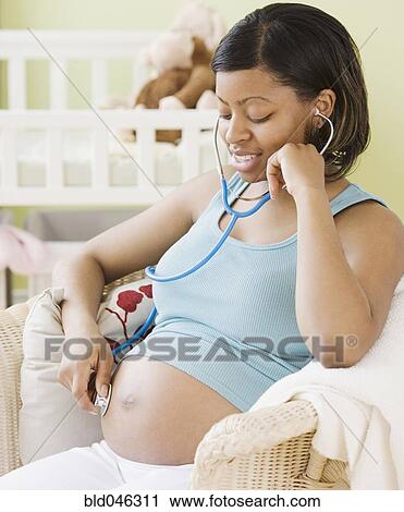 Stock Image - Pregnant African American woman listening to belly. Fotosearch