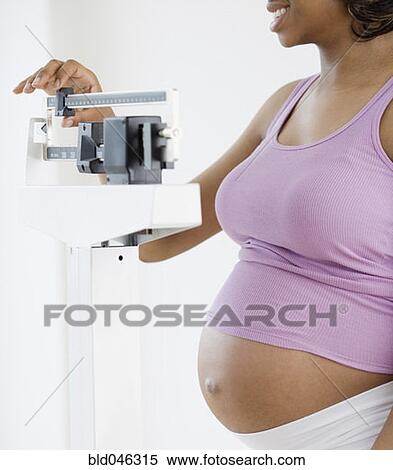 Stock Photography - Pregnant African American woman standing on scale. Fotosearch