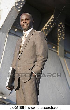 Stock Image - African American businessman holding laptop. Fotosearch