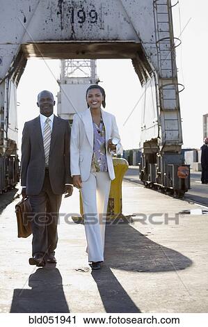 Stock Image - African American businesspeople walking on commercial pier. Fotosearch