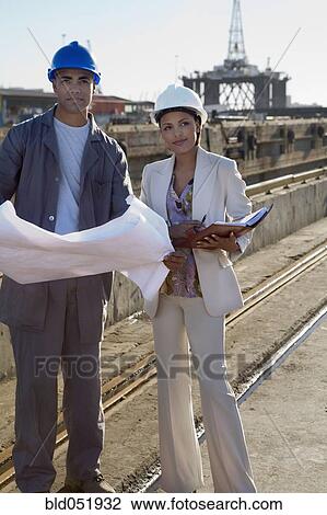 Stock Image - African American businesswoman and construction worker with blueprints. Fotosearch