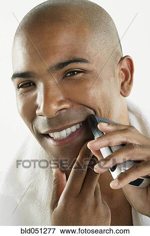 Stock Photo - African American man shaving face with electric razor. Fotosearch