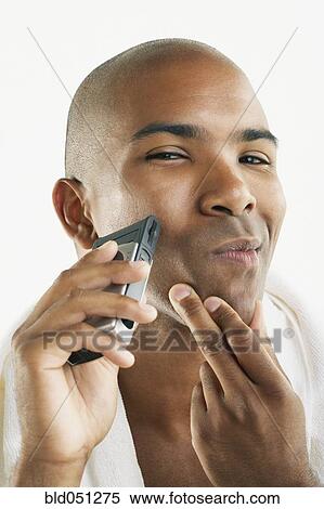 Stock Photography - African American man shaving face with electric razor. Fotosearch