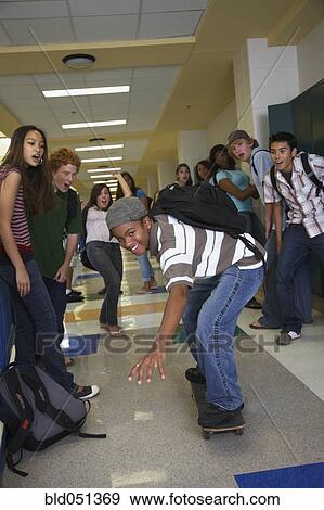 Stock Photo - African American teenaged boy riding skateboard in school hallway. Fotosearch