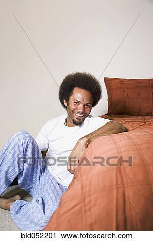 Stock Image - African man sitting next to bed. Fotosearch