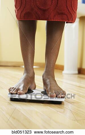 Stock Image - African man standing on scale. Fotosearch