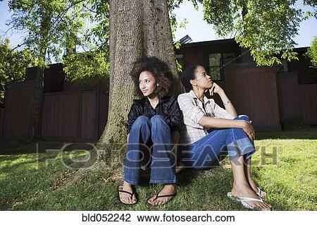 Stock Image - African women sitting against tree. Fotosearch