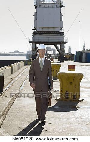 Stock Image - Asian businessman walking on commercial pier. Fotosearch