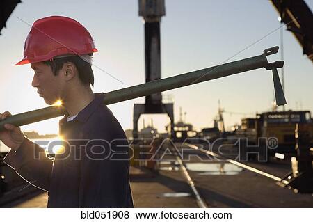 Stock Photo - Asian male construction worker carrying pipe. Fotosearch
