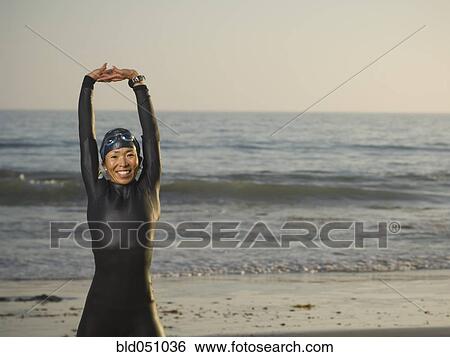 Stock Photograph - Asian woman stretching in wetsuit and goggles. Fotosearch