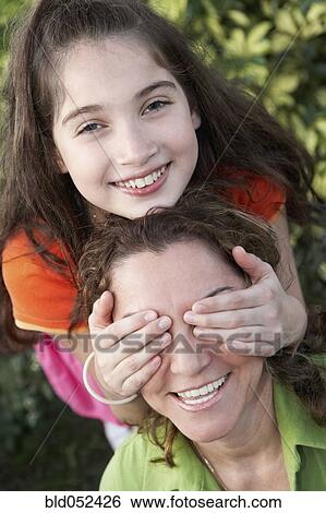 Stock Photograph - Hispanic girl covering mother’s eyes. Fotosearch
