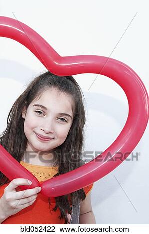 Stock Image - Hispanic girl holding heart-shaped balloon. Fotosearch