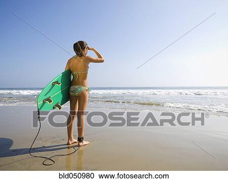 Stock Image - Hispanic girl holding surfboard. Fotosearch