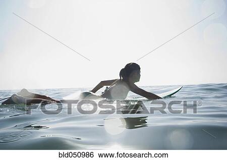 Stock Photograph - Hispanic girl paddling on surfboard. Fotosearch