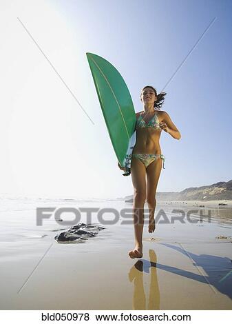 Stock Photo - Hispanic girl running with surfboard. Fotosearch