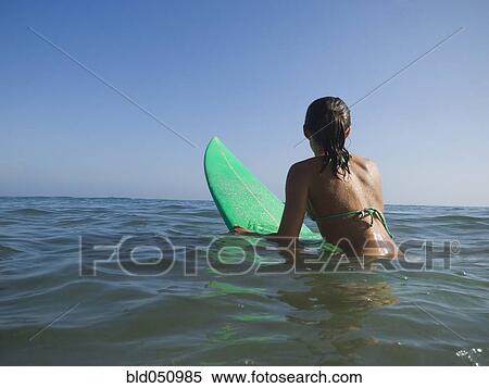 Stock Photography - Hispanic girl sitting on surfboard. Fotosearch