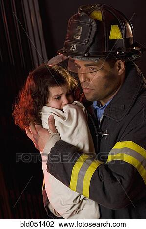 Stock Image - Hispanic male firefighter holding child. Fotosearch