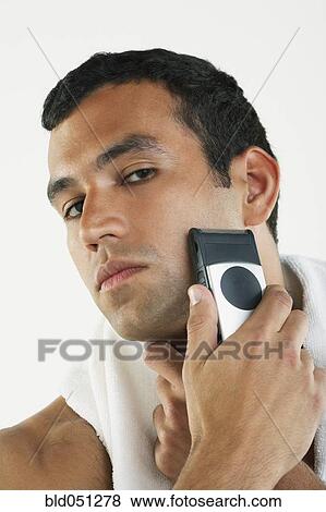 Stock Photo - Hispanic man shaving face with electric razor. Fotosearch