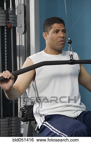 Stock Photograph - Hispanic man using weight machine. Fotosearch