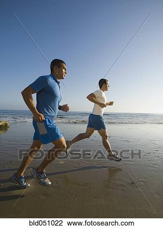 Stock Image - Hispanic men running at beach. Fotosearch