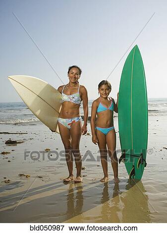 Stock Photo - Hispanic mother and daughter holding surfboards. Fotosearch