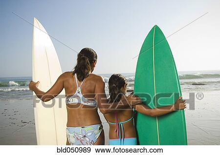 Stock Photo - Hispanic mother and daughter holding surfboards. Fotosearch