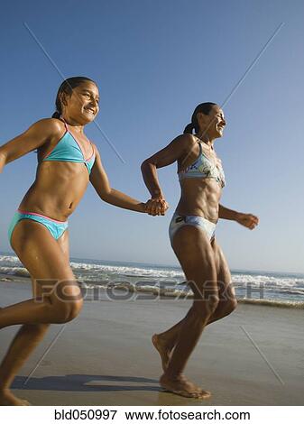 Stock Photo - Hispanic mother and daughter running at beach. Fotosearch