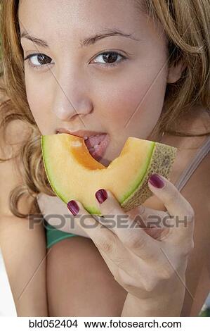 Picture - Hispanic woman eating melon slice. Fotosearch